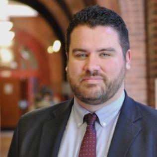 image of franz set against a door and brick wall. Franz is wearing a blazer.