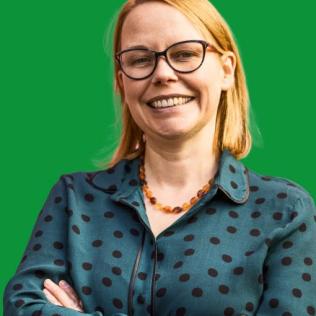 image of laura in front of a green background. Laura has on a polka dot button up and glasses.