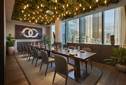 Private dining room at Los Mochis London set for a group event, with a long wooden table, Edison bulb chandelier, living green ceiling, and city skyline views.