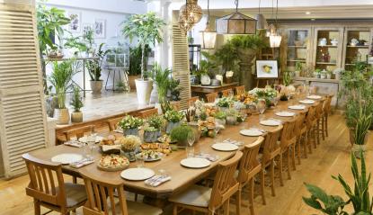 Picture of the wooden, custom-built dining table at The Conservatory at the Langham in London. An airy and inviting space decked out with lush greenery and grand features.