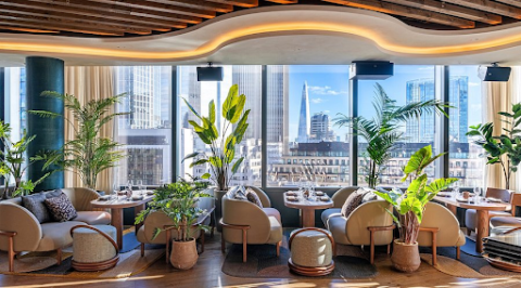 Interior of Los Mochis London restaurant featuring curved lounge seating, tropical plants, and floor-to-ceiling windows overlooking the London skyline.